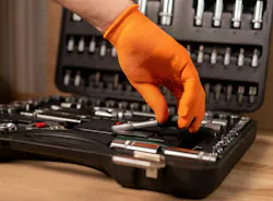 Male hand in building glove with socket ratchet handle, taken from toolbox. Industrial metal tool, close up on wooden background.