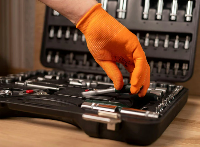 Male hand in building glove with socket ratchet handle, taken from toolbox. Industrial metal tool, close up on wooden background.