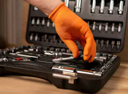 Male hand in building glove with socket ratchet handle, taken from toolbox. Industrial metal tool, close up on wooden background.