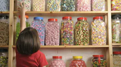 Young girl looking at rows of sweets in shop and reaching for a jar on the top shelf