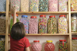 Young girl looking at rows of sweets in shop and reaching for a jar on the top shelf