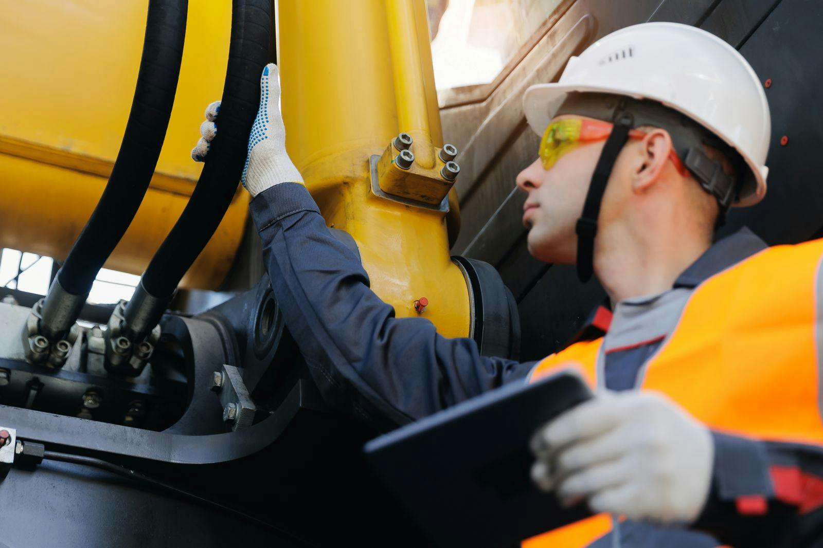 Male engineer inspecting machinery hydraulic hose systems on construction site.