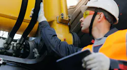 Male engineer inspecting machinery hydraulic hose systems on construction site.