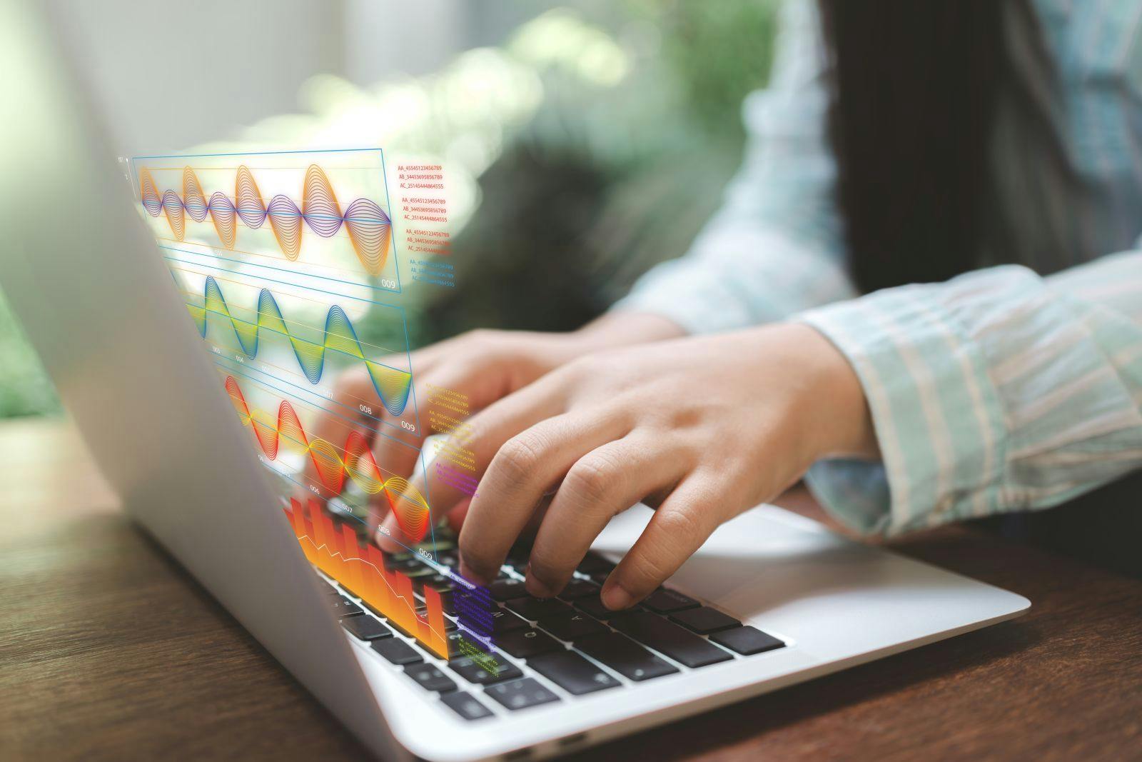 Hands typing on a laptop with holographic charts. Real-time analytics turn numbers into AI insights, powering forecasting and decisions. Modern workflow where algorithms and dashboards reveal trends