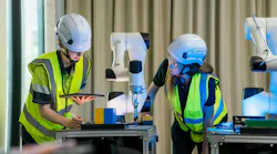 Two people wearing yellow vests and helmets are working on a robot.